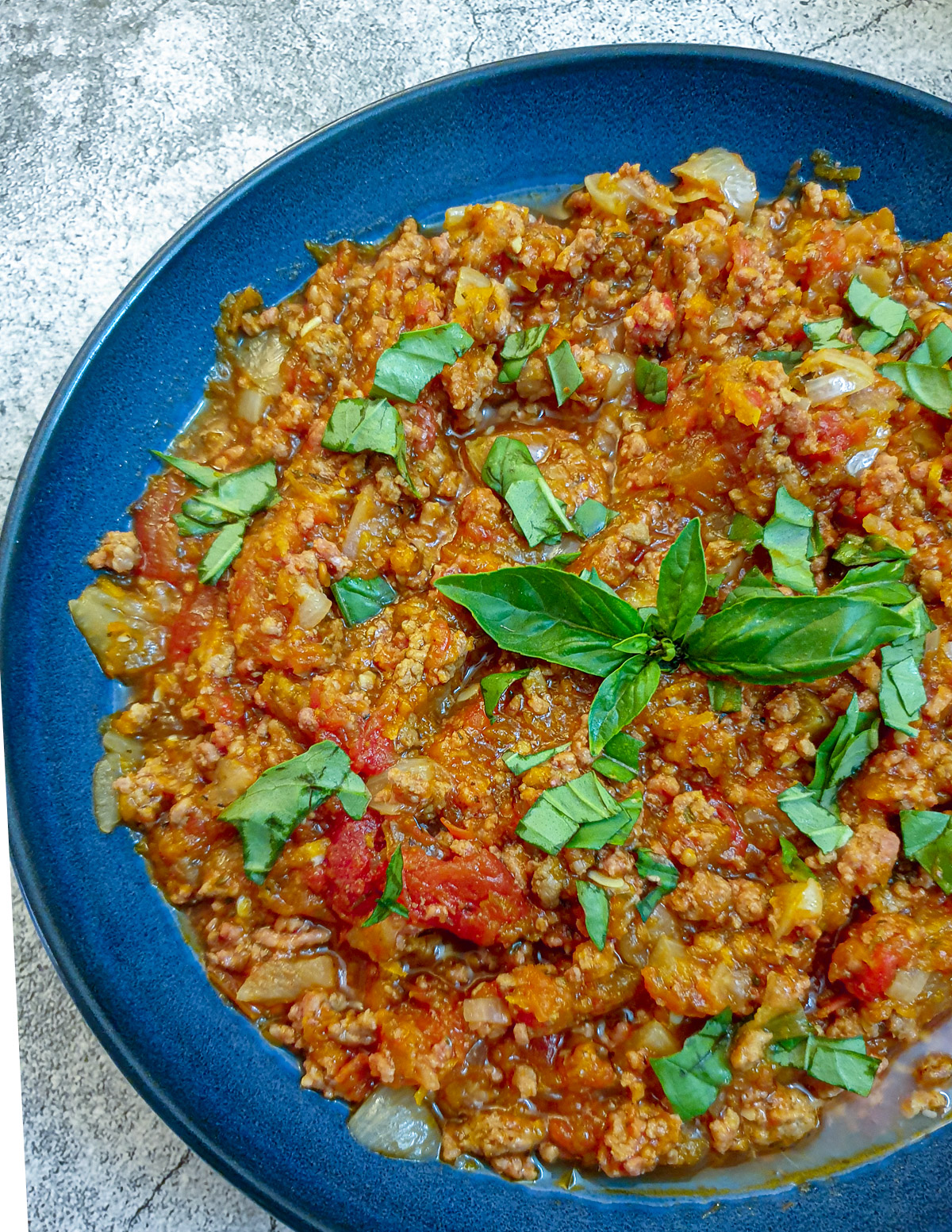 Close up of a dish of bolognese sauce garnished with basil.