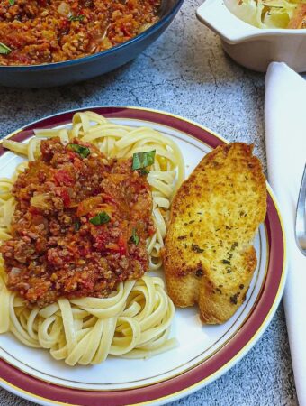 A plate of spaghetti with bolognese sauce and garlic bread.