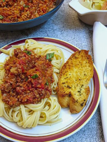 A plate of spaghetti with bolognese sauce and garlic bread.