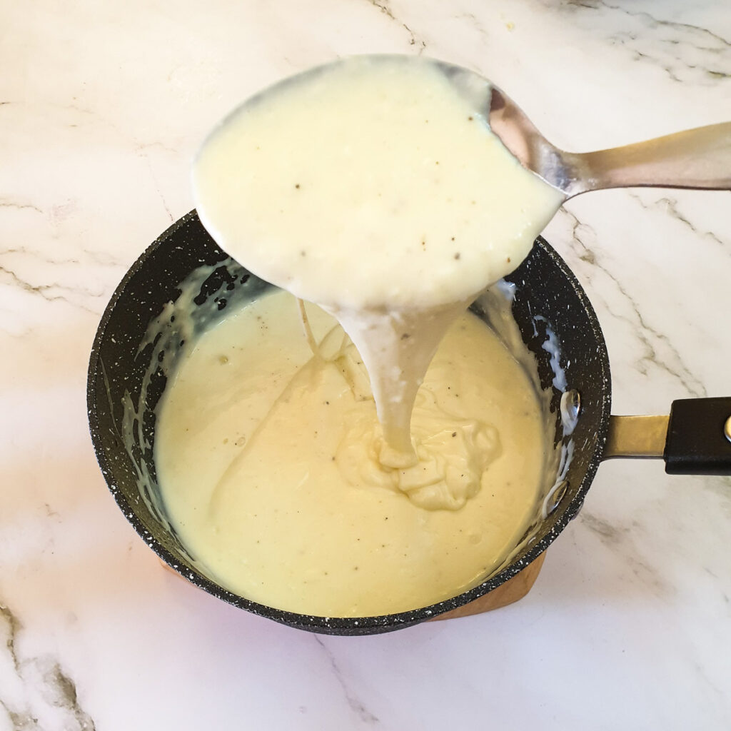 A spoonful of cheese sauce held over a saucepan.