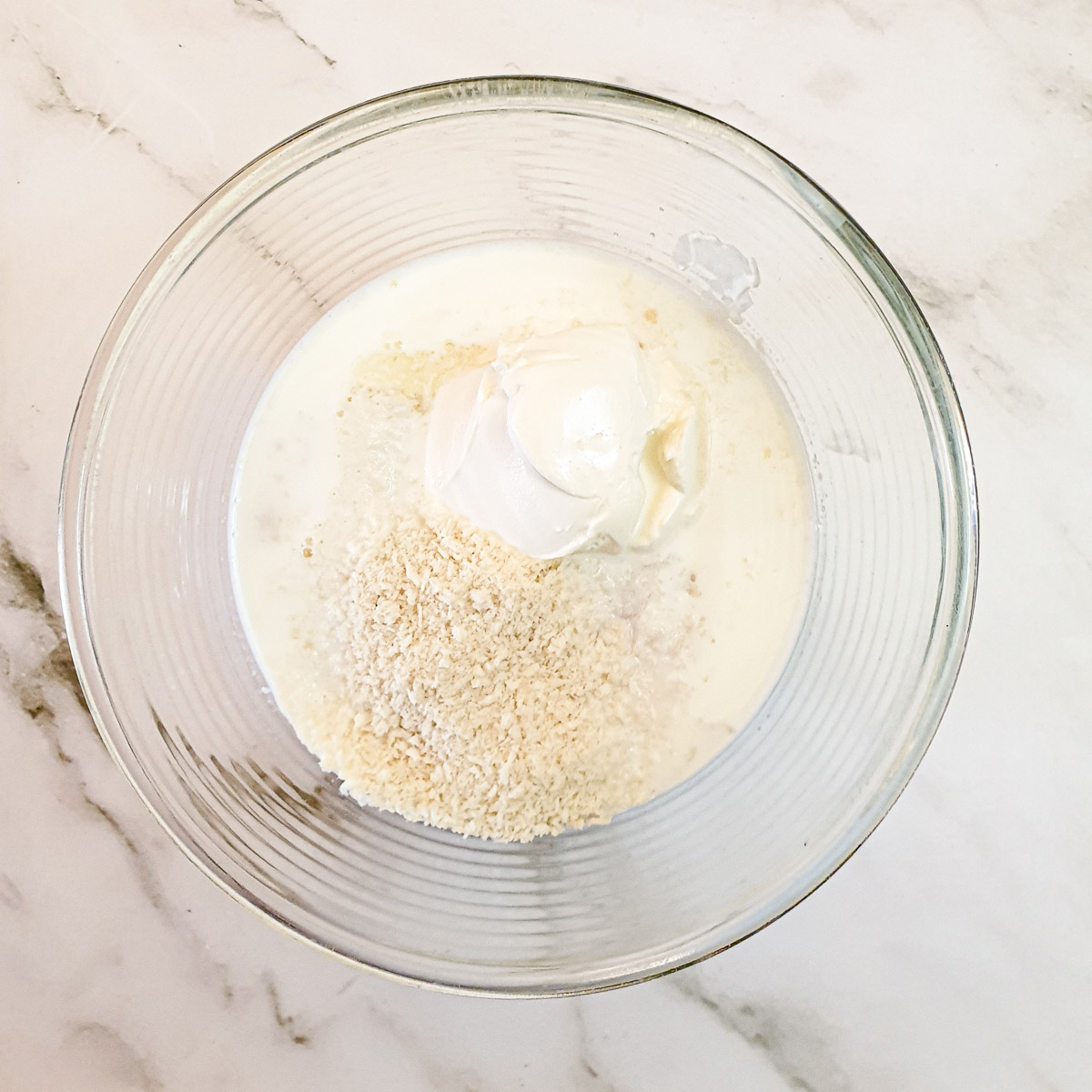 Milk, cream cheese, eggs and breadcrumbs in a glass mixing bowl.