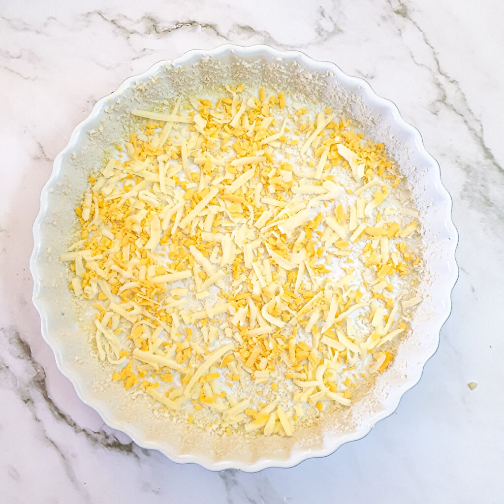 A round baking dish coated with oil and breadcrumbs with grated cheese in the base.