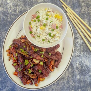 A plate of dragon beef with a dish of chinese fried rice.