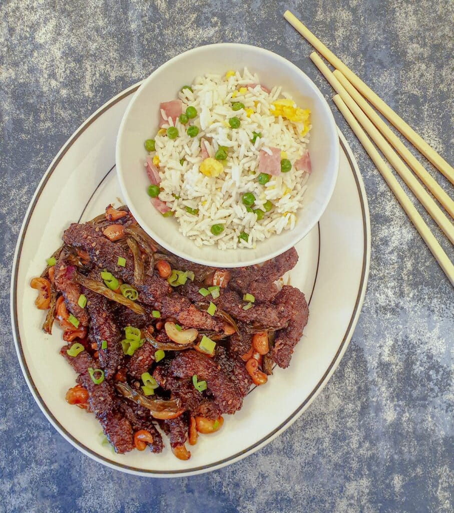 A plate of dragon beef with a dish of chinese fried rice.