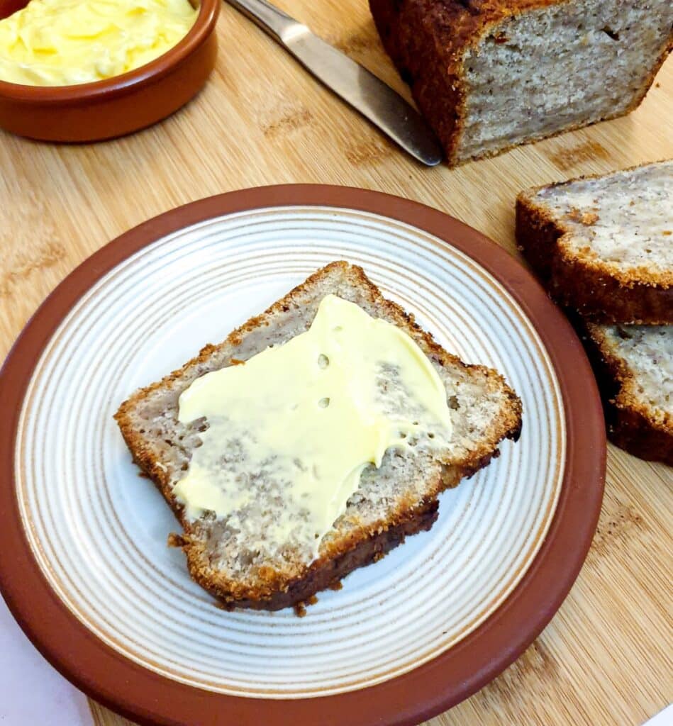 A buttered slice of pear and banana loaf on a plate.