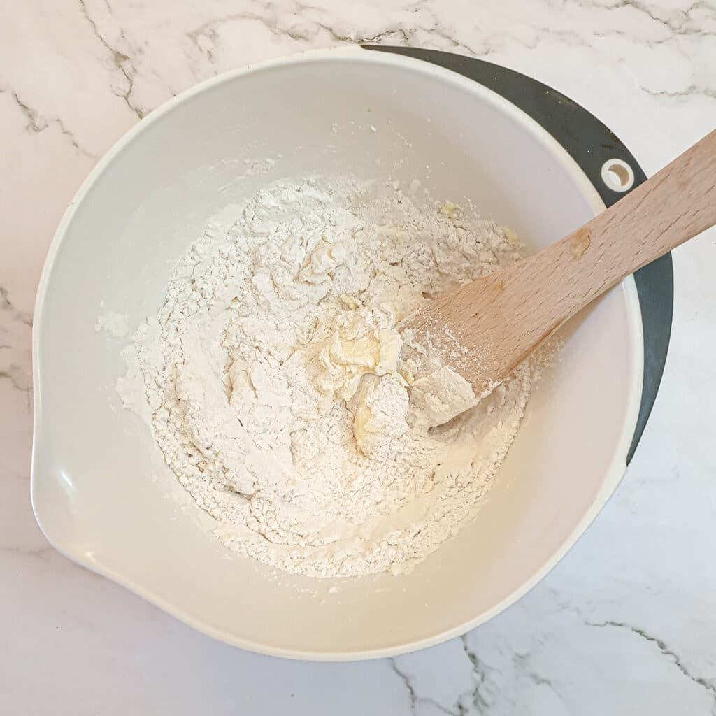 Flour added to creamed butter and sugar in a mixing bowl.