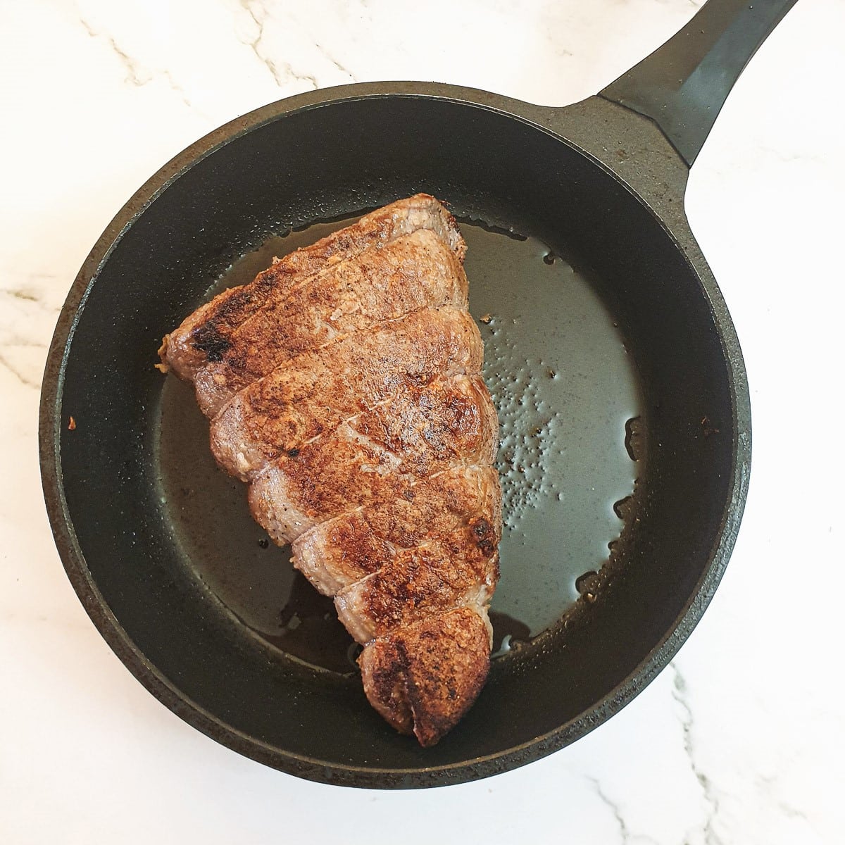 A joint of beef being browned in a frying pan.