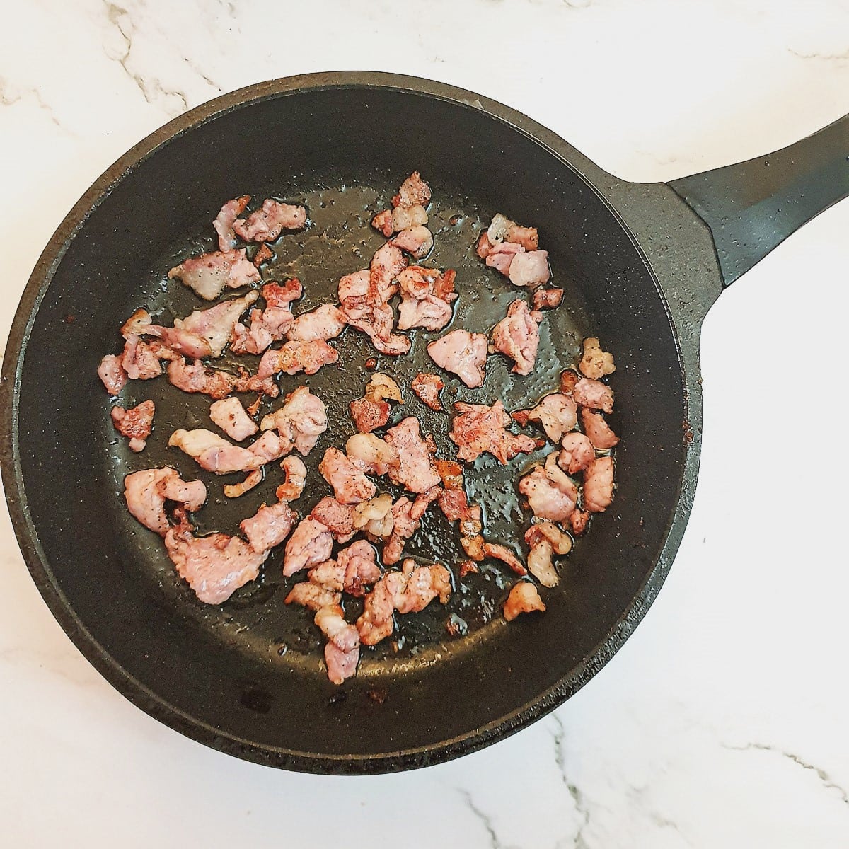 Pieces of bacon being browned in a frying pan.