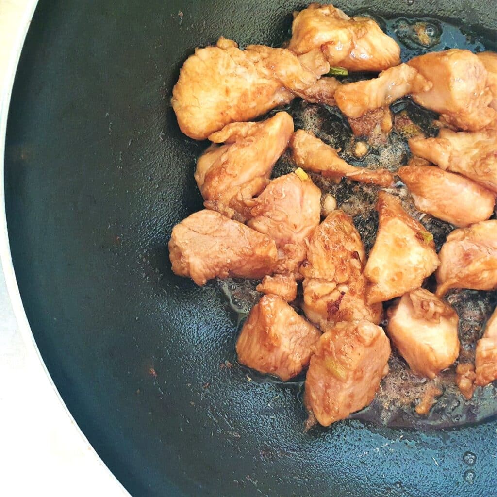 Chicken pieces being browned in a frying pan.