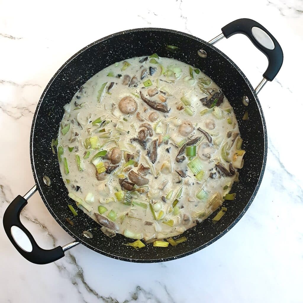 Leeks and onions in a creamy sauce, in a frying pan.