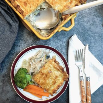 A slice of chicken, leek and mushroom pie on a plate with vegetables.
