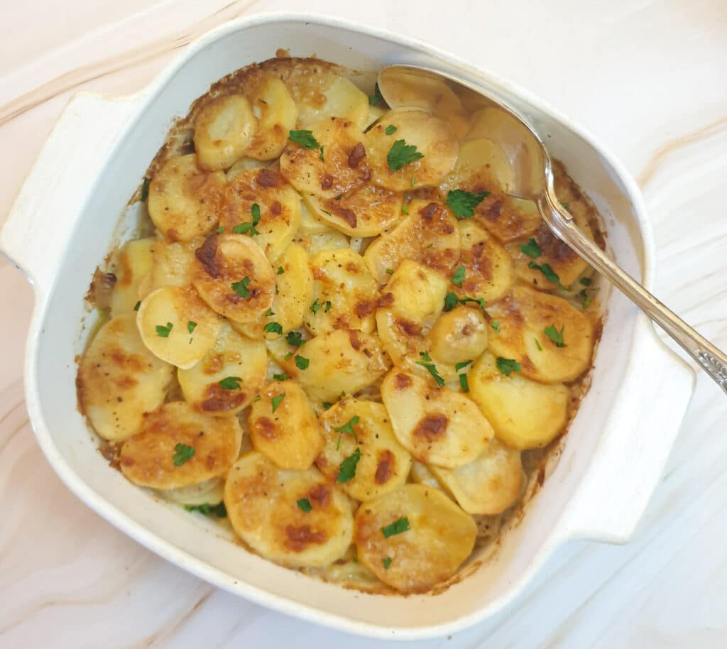 A dish of crispy boulangere potatoes with a serving spoon.