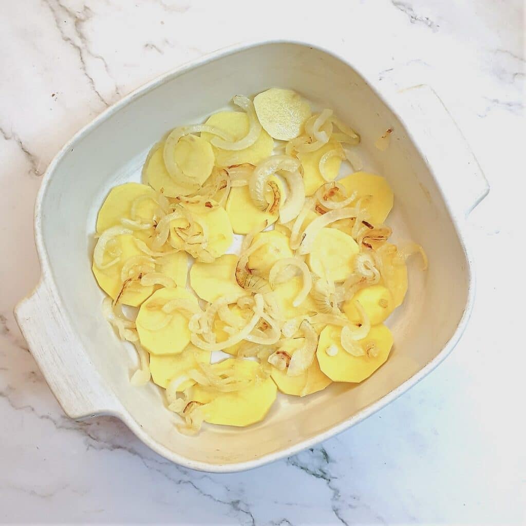 A layer of sliced potatoes and onions in a baking dish.