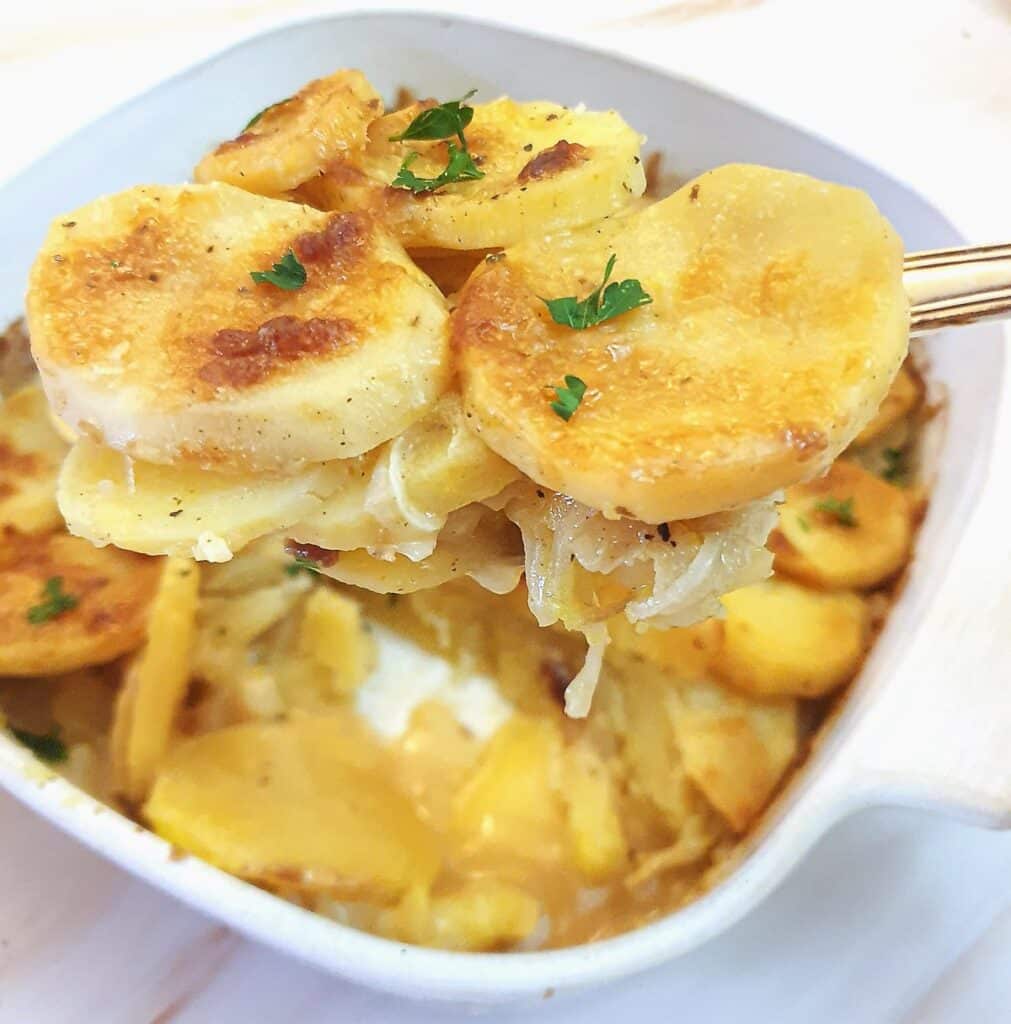 A spoonful of boulangere potatoes being lifted from a serving dish.