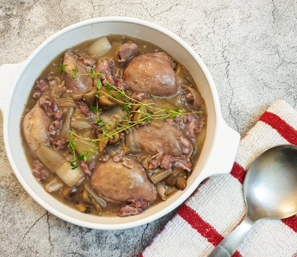 A serving dish of coq au vin with a spoon on a towel.