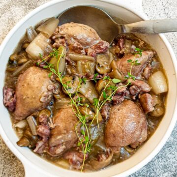 A dish of coq au vin garnished with a sprig of fresh thyme.