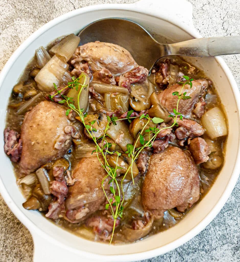 A dish of coq au vin garnished with a sprig of fresh thyme.