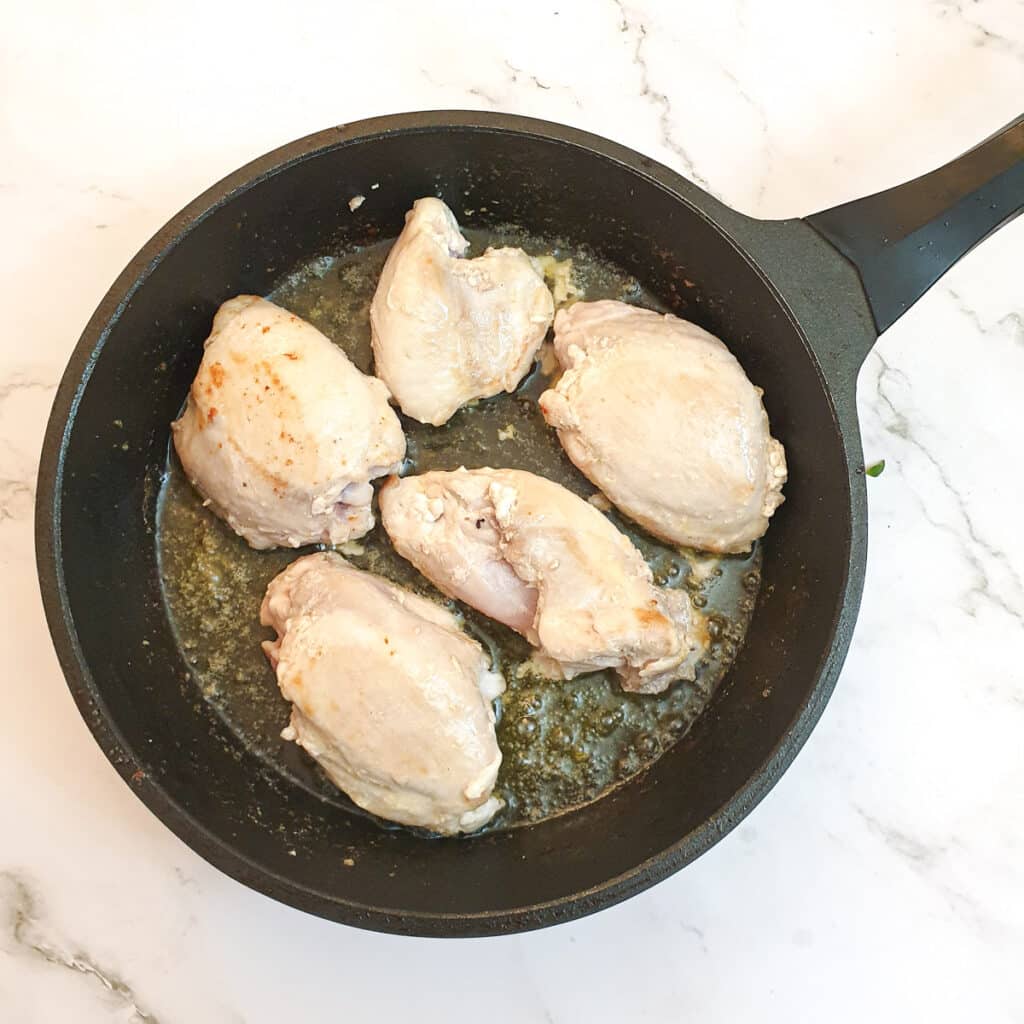 Chicken pieces browning in a frying pan.