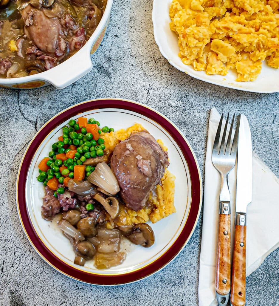 Coq au vin on a plate with sweet potato mash, peas and carrots.