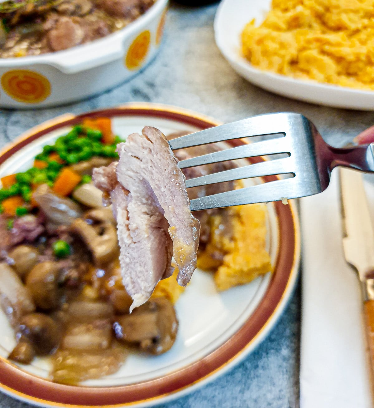 A piece of chicken on a fork held over a plate of coq au vin.