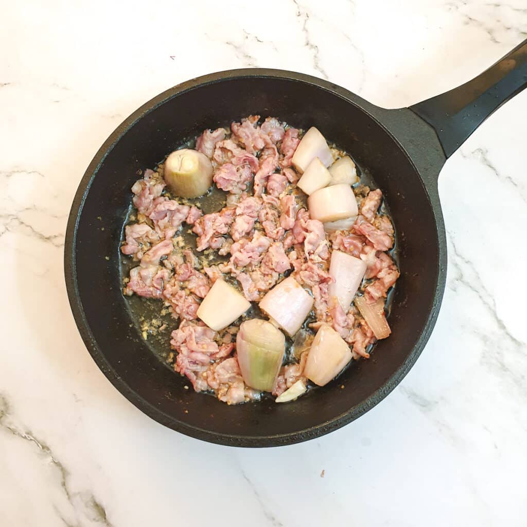 Bacon and shallots browning in a frying pan.