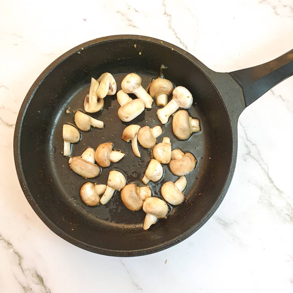 Mushrooms browning in a frying pan.