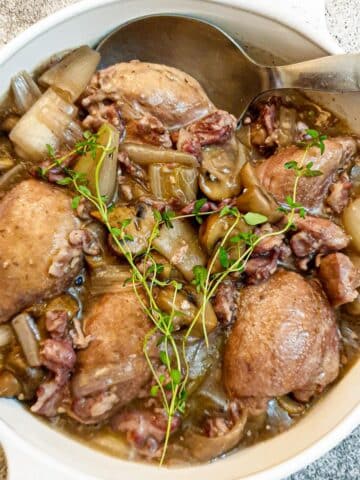 A dish of coq au vin garnished with a sprig of fresh thyme.