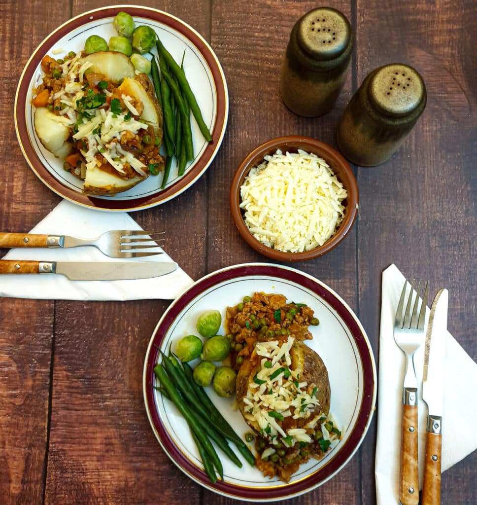 Overhead shot of 2 plates with baked potatoes covered in savoury mince.