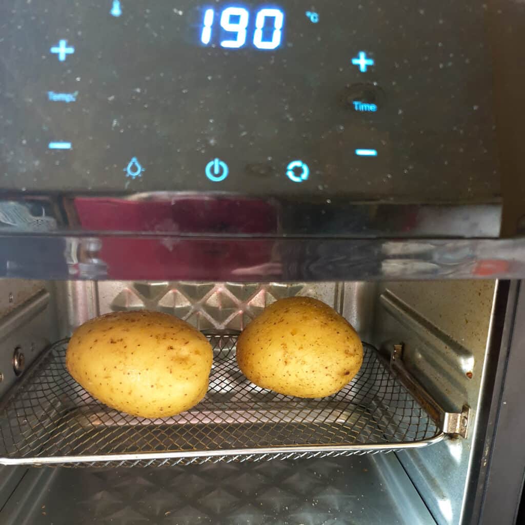 Two baked potatoes in an air-fryer oven.