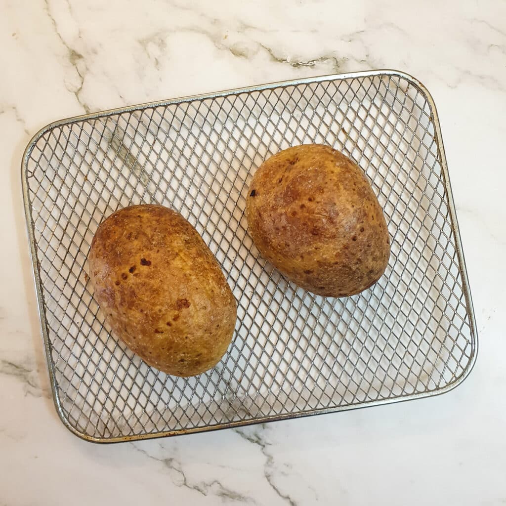 Two baked potatoes on an air-fryer oven rack.