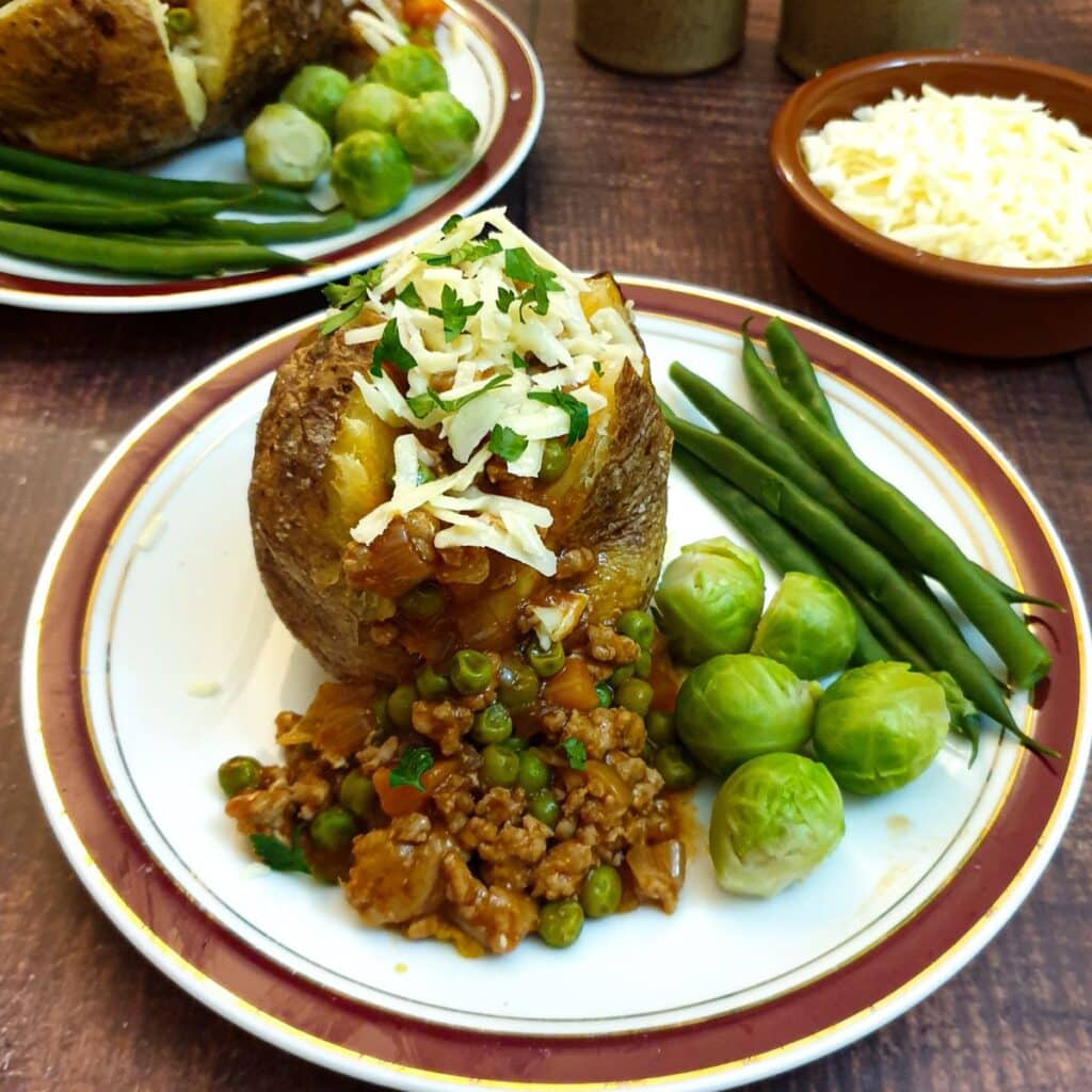 A baked potato covered in savoury mince on a plate with steamed vegetables.