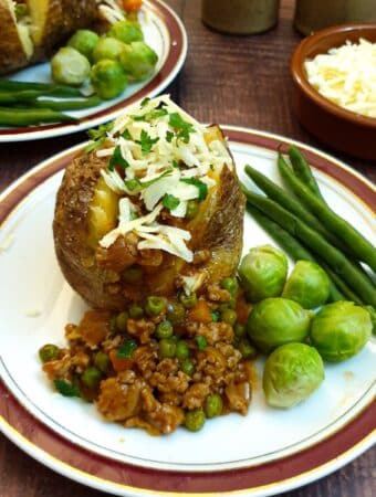 A baked potato covered in savoury mince on a plate with steamed vegetables.