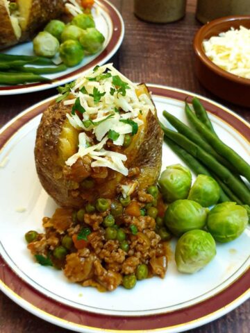 A baked potato covered in savoury mince on a plate with steamed vegetables.