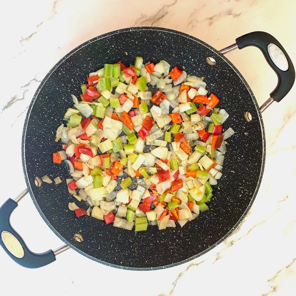 Onions, celery and red peppers being softened in a frying pan.