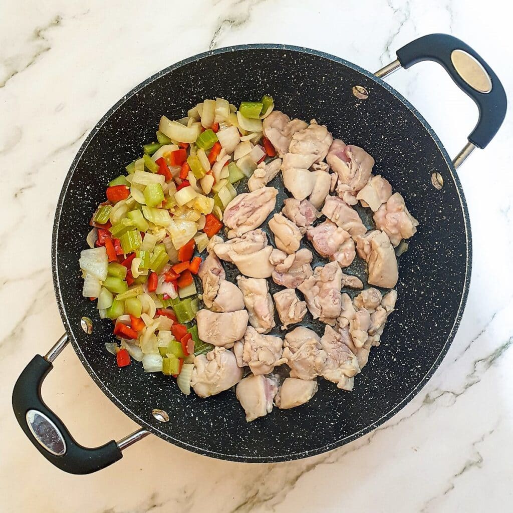 Chicken pieces being browned in a pan.
