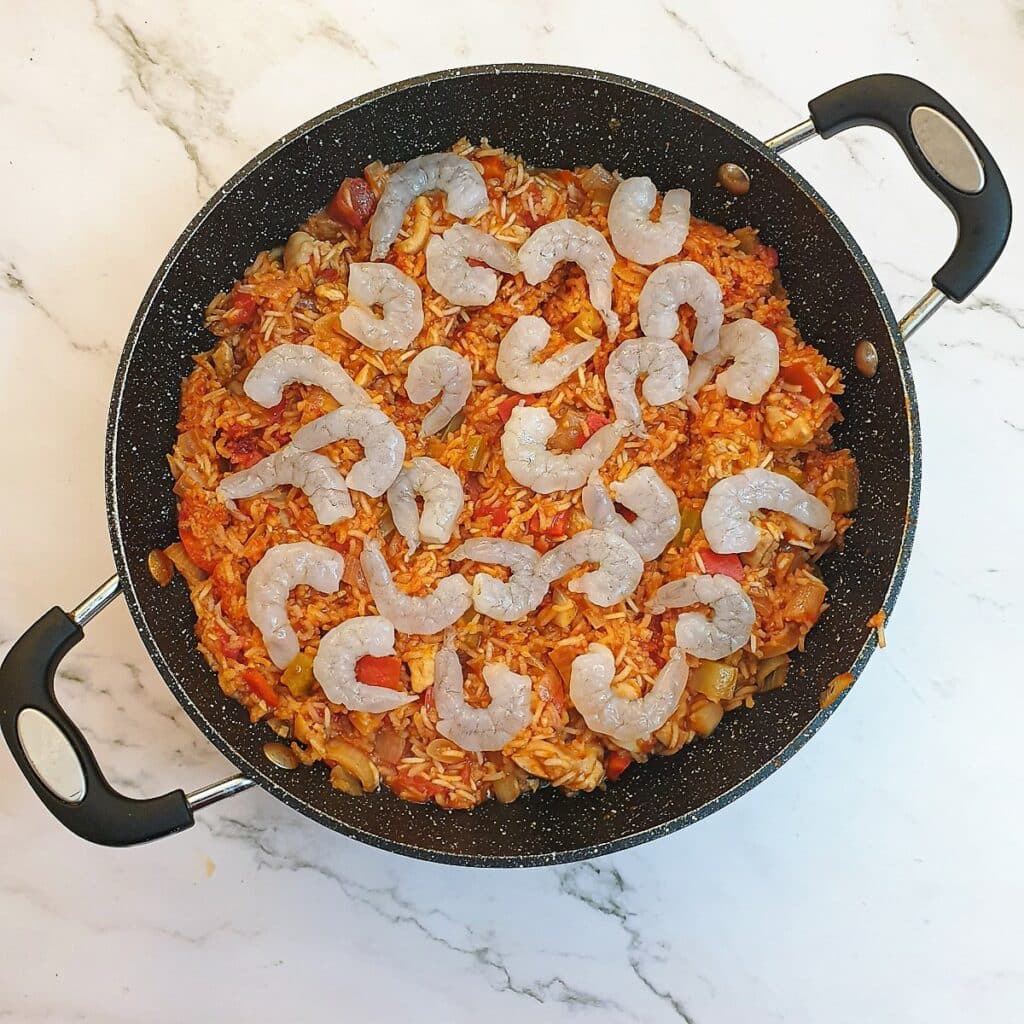 Creole jambalaya in a pan, covered with raw prawns.