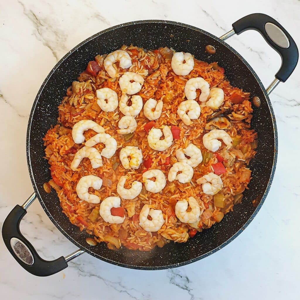 Creole jambalaya in a pan, covered with cooked prawns.