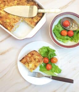 A slice of crustless ham and cheese quiche on a plate with tomatoes and lettuce, shot from above.