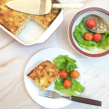 A slice of crustless ham and cheese quiche on a plate with tomatoes and lettuce, shot from above.