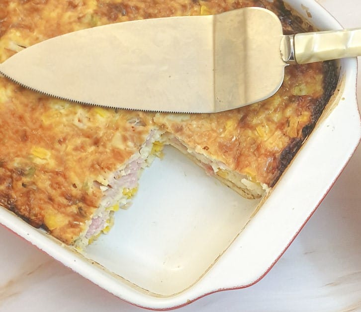 Ham, cheese and sweetcorn quiche in a dish with a corner slice removed.
