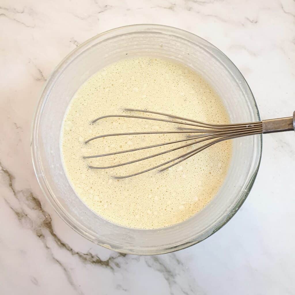 Eggs, milk, cream and flour being whisked in a mixing bowl.