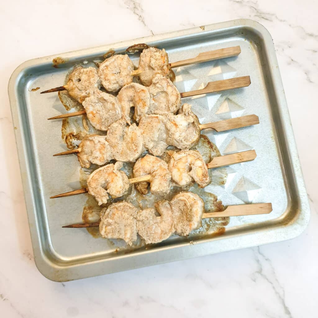 Half-cooked prawn skewers on an air fryer tray.