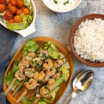 A plate of curried prawn skewere with a bowl of rice and cucumber raita.