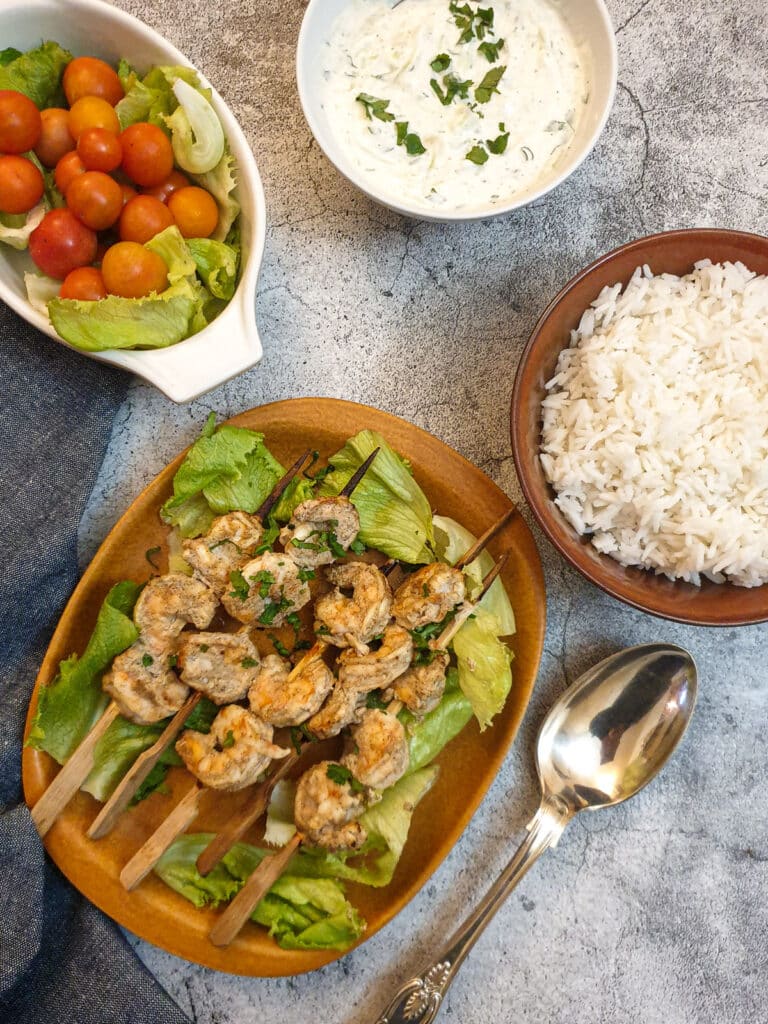 A plate of curried prawn skewere with a bowl of rice and cucumber raira