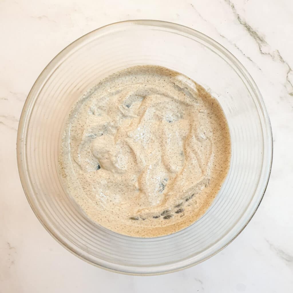 A glass bowl containing prawns submerged in a marinade.