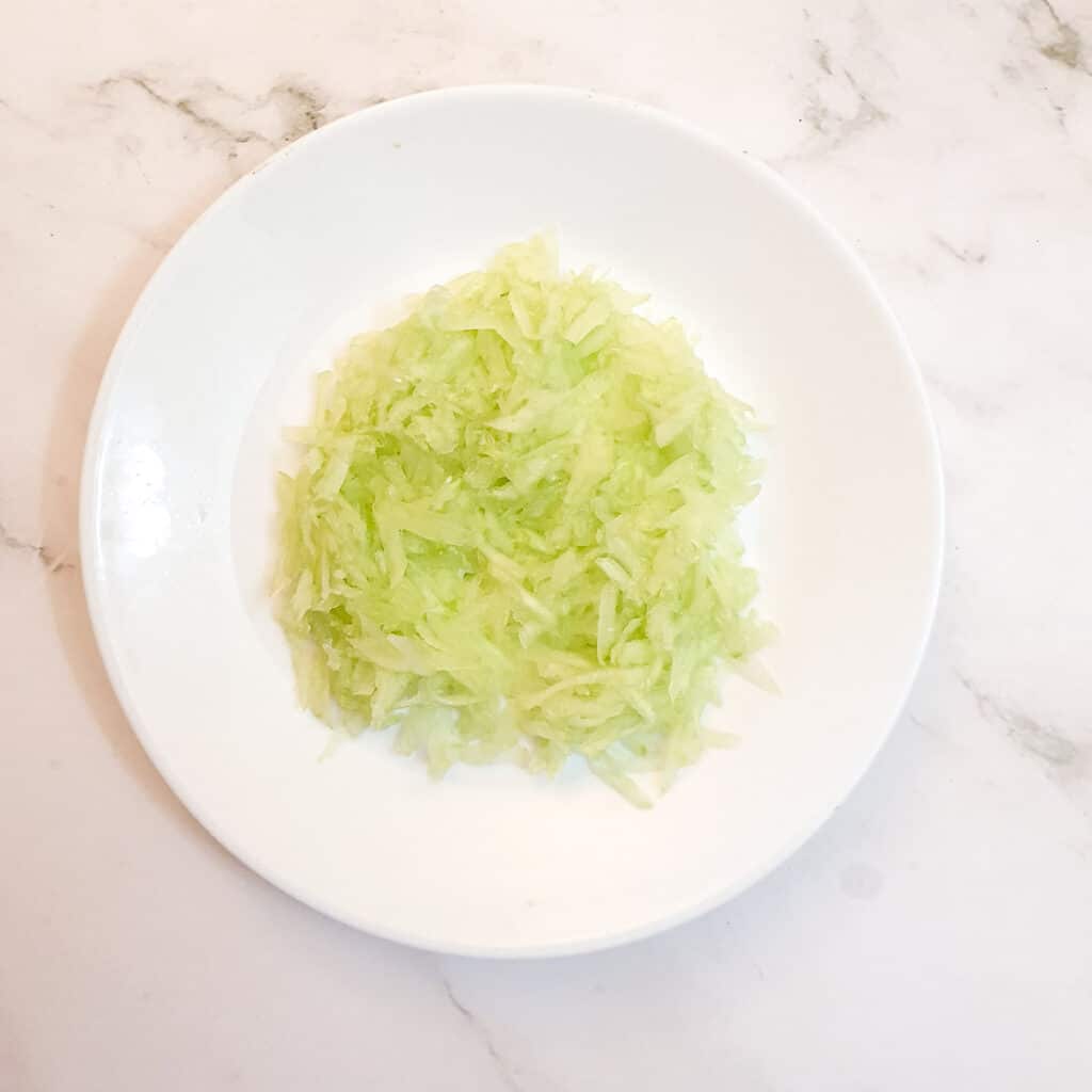 A pile of grated cucumber on a white plate.