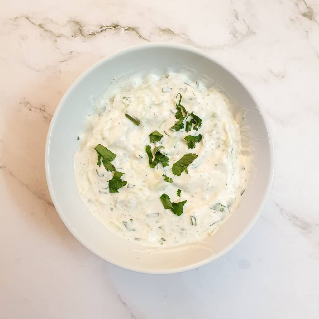 A dish of cucumber raita garnished with chopped coriander.