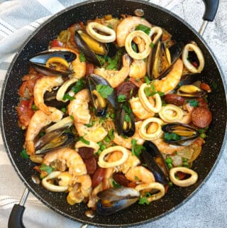 A pan of Spanish paella garnished with prawn, mussels and calamari rings.