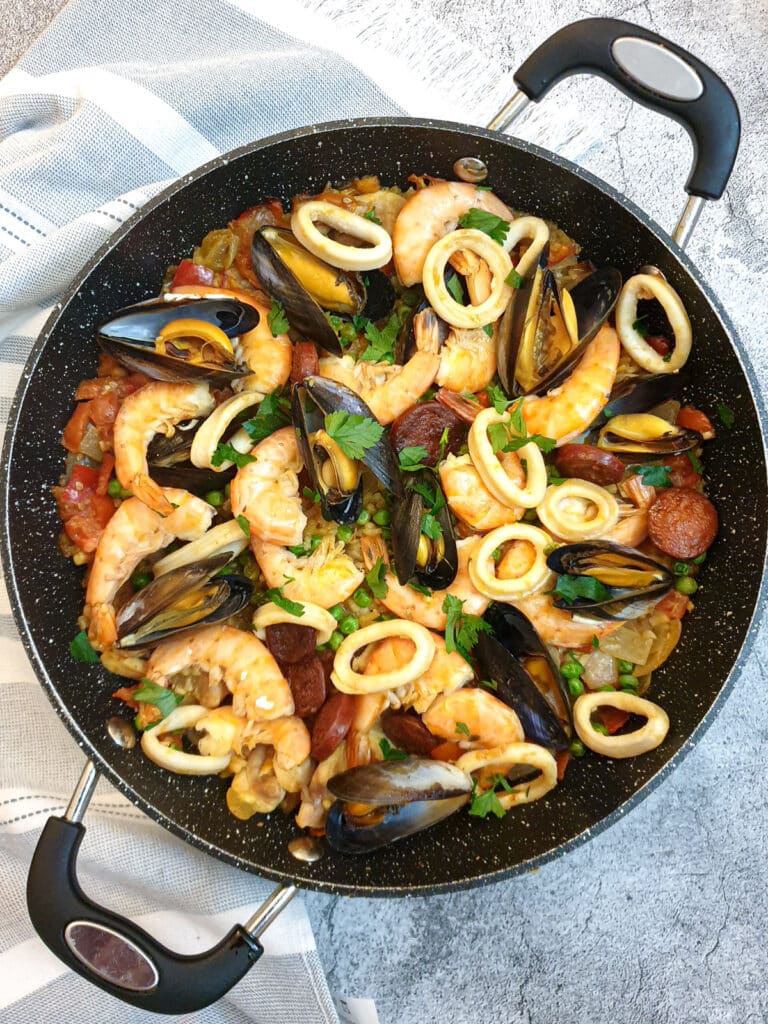 A pan of Spanish paella garnished with prawn, mussels and calamari rings.
