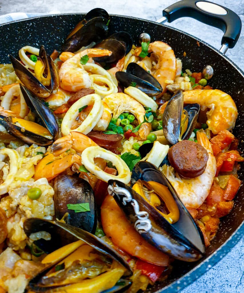 Prawns, mussels, calamari, chorizo and peas on top of a bed of rice in a saute pan.